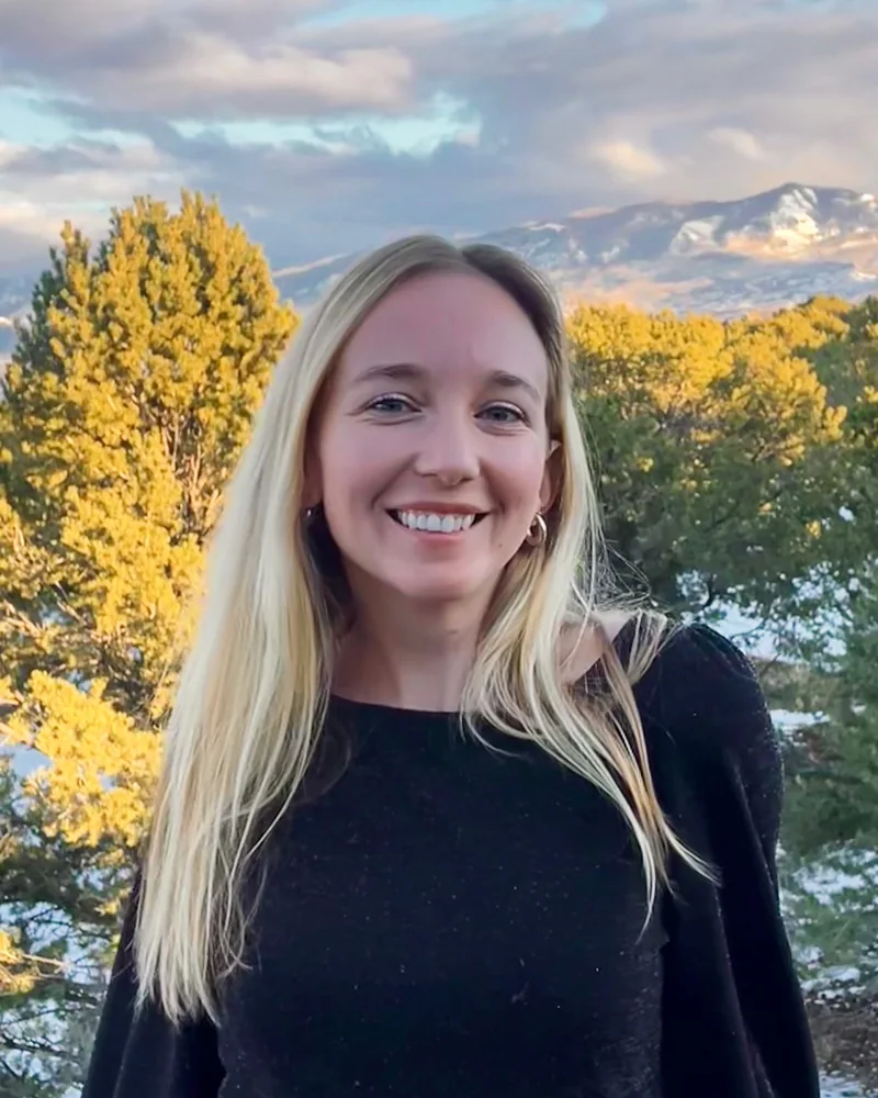 Madeline Sparks smiling outdoors with mountains and evergreen trees behind her